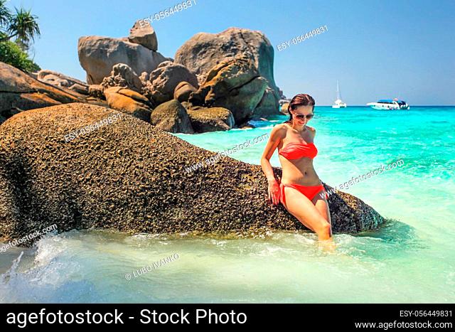 Young woman in red bikini sitting on huge rock in a nice turquoise sea. Similan islands, Thailand