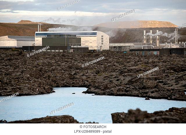 Geothermal power factory, surrounded by rocky landscape with a lake