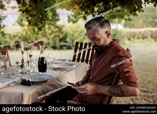 Man sitting at table in garden and using cell phone