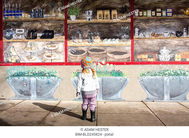 Caucasian girl standing on sidewalk admiring mural on wall