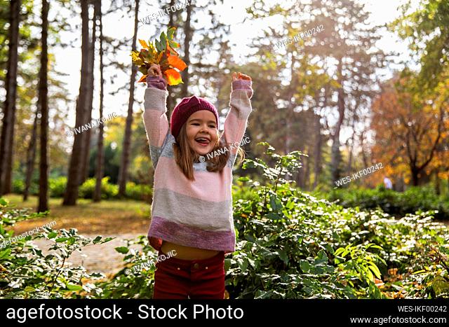 Cheerful girl playing with leaves at park