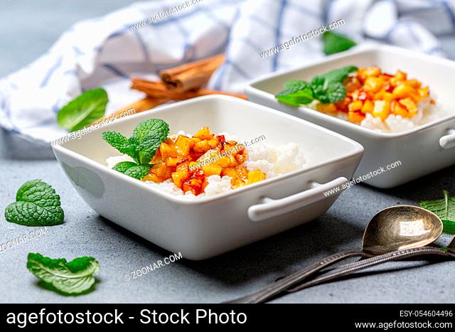 Traditional rice porridge with almond milk with caramelized apples in white bowls on a textured gray background, selective focus