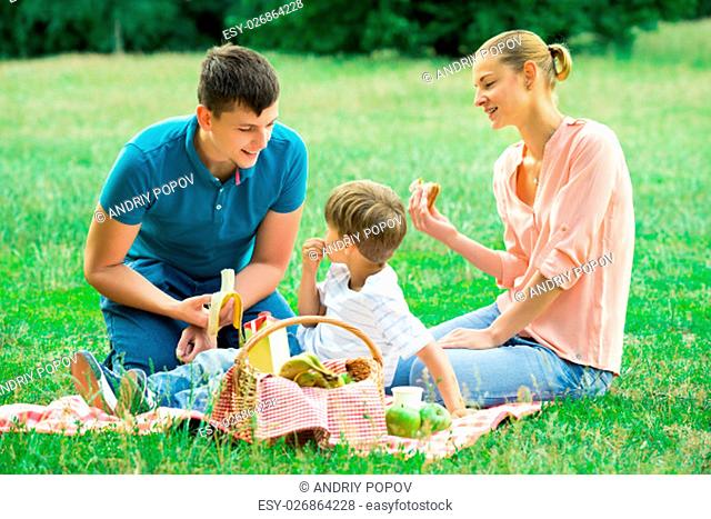 Young Happy Family Enjoying Breakfast At Picnic In The Park