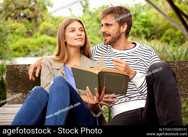 Couple reading book while sitting on bench