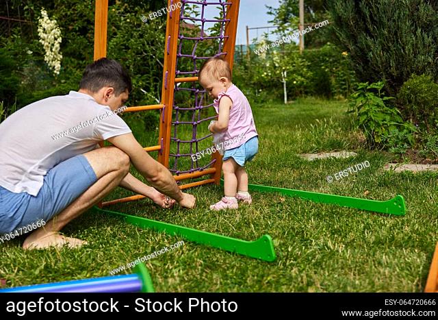 Dad with little child girl daughter collects wooden home sports complex outdoor. assembly process