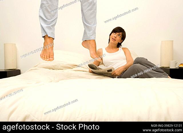 Woman watching husband jump on bed