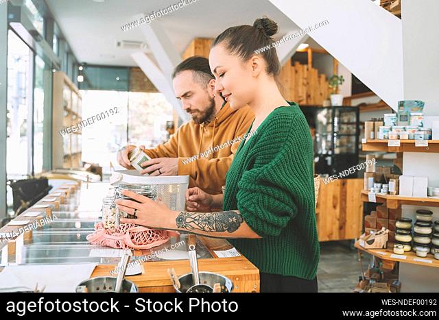 Smiling woman arranging jars in mesh bag on counter at store