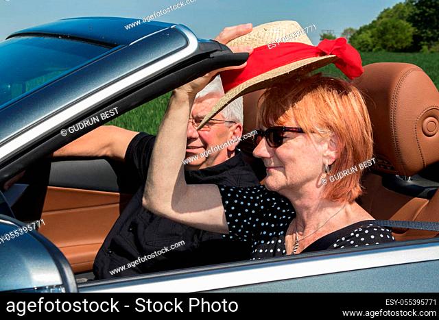 Older couple drives with a luxury convertible car on a sunny day