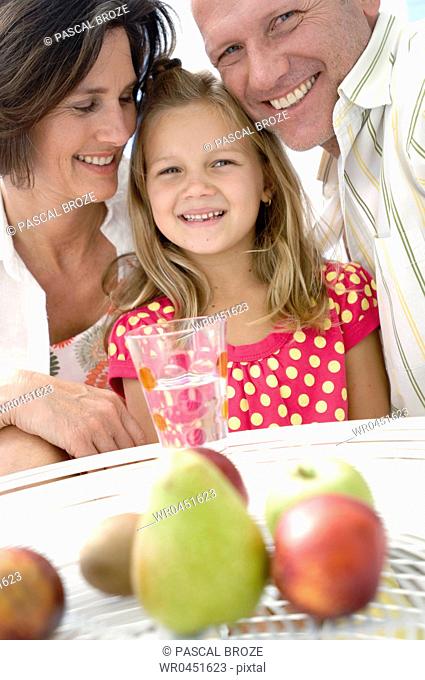 Close-up of a mid adult couple and their daughter smiling with fruits before them