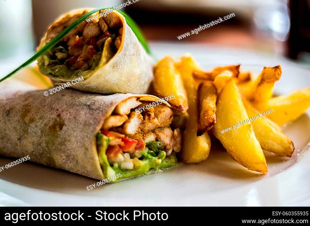 Tasty wraps with chicken, avocado, lettuce and french fries on a plate. Selective focus