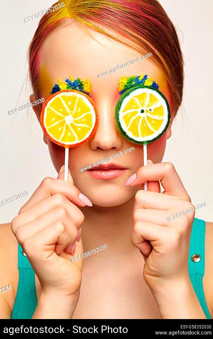 Teenager girl with unusual face art make-up . Child with lollipops in hands closing eyes. Sweet tooth concept
