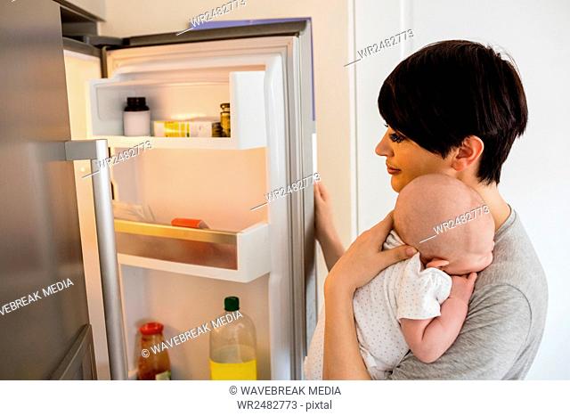 Mother with her baby looking into refrigerator in kitchen