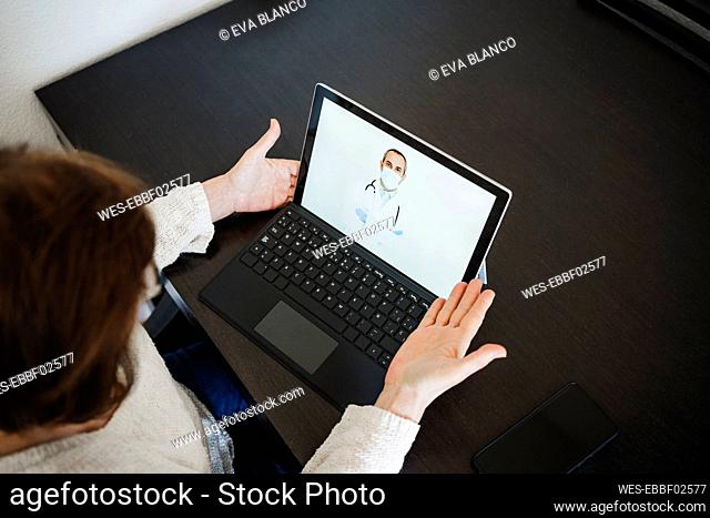 Senior woman with laptop discussing with doctor through video call at table