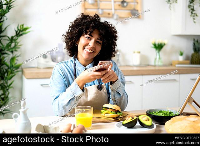 Portrait of young woman using smart phone at kitchen table