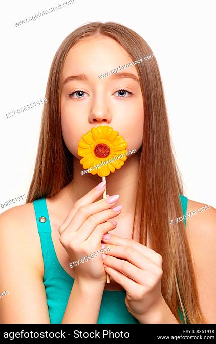 Teenager girl with flower lollipop in hands closing mouth. Sweet tooth concept