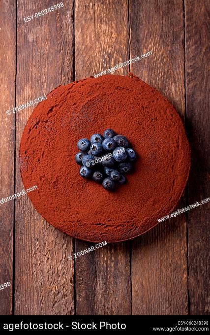 Chocolate cake with cacao powder and blueberries on a wooden background. top view