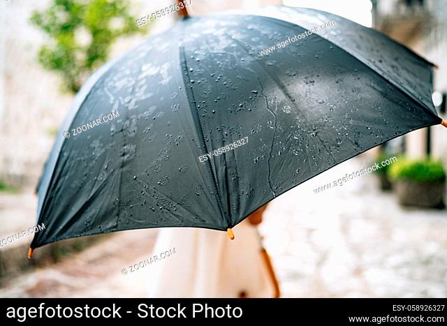 The child poses with an umbrella. A little girl in dress stands outside under an umbrella black during the rain