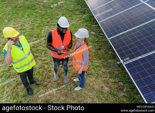 Engineer and coworker discussing over tablet PC standing by solar panels