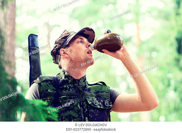 war, hiking, army and people concept - young soldier or ranger with gun drinking from flask in forest