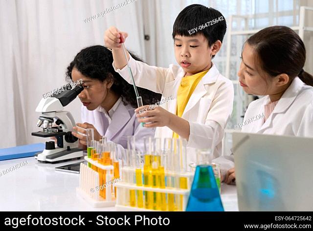 Pupil wearing white laboratory coat and learning science experiment by using eye dropper for dropping blue liquid to test tube in science laboratory room with...