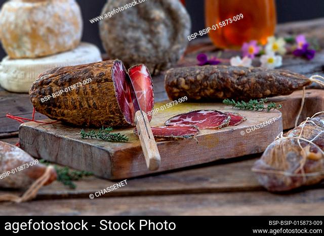 Several variety of traditional Corsican charcuterie with an olive branch and black olives onrustic background