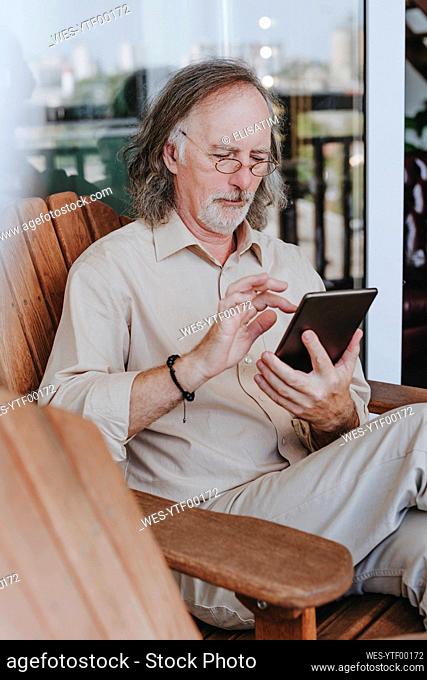Senior man sitting on chair and using tablet PC at home terrace