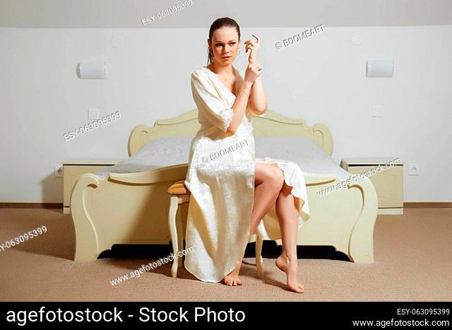 pretty young lady in bedroom in silk peignoir sits on the couch near the bed