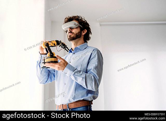 Businessman wearing VR glasses holding robotic arm in office