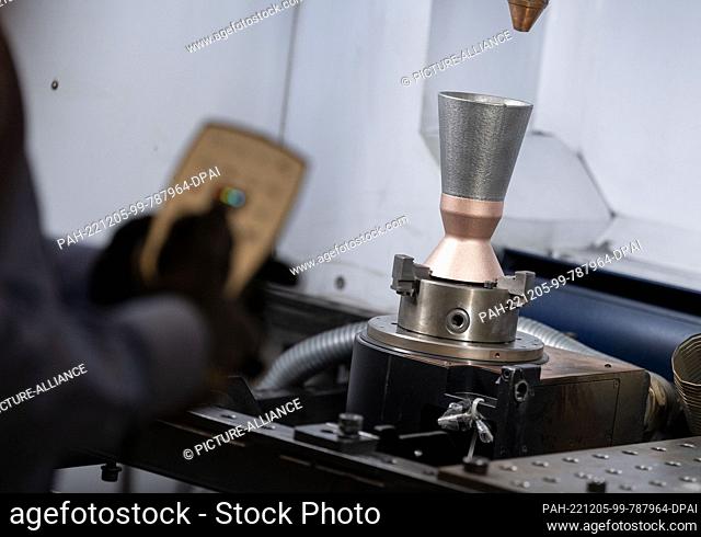 PRODUCTION - 30 November 2022, Baden-Wuerttemberg, Ditzingen: An employee of laser specialist Trumpf uses a model of a thruster for space shuttles to...