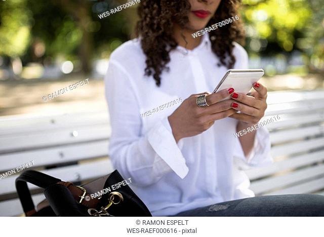 Young woman sitting on park bench using her smartphone, close-up