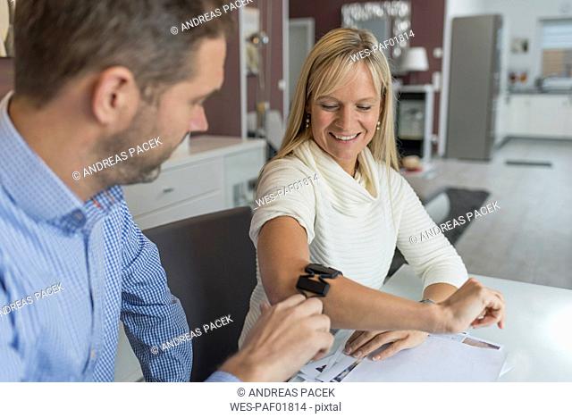 Man and smiling woman with wearable at her arm at desk