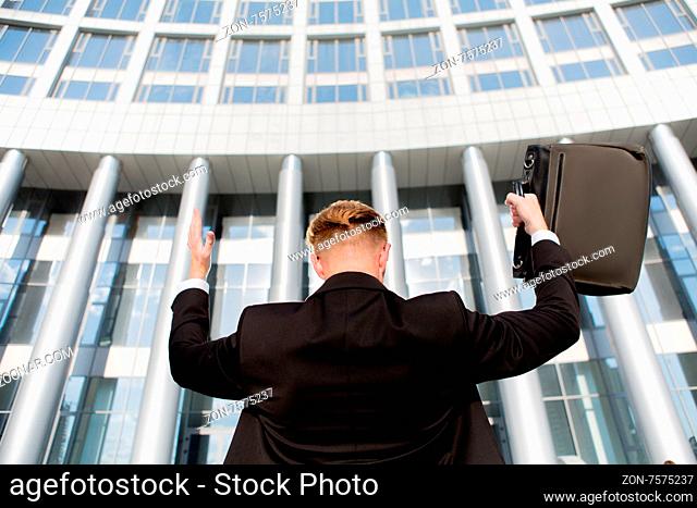 Portrait of king of the world with his hands raised. Young successful businessman in front of the office building with brief case
