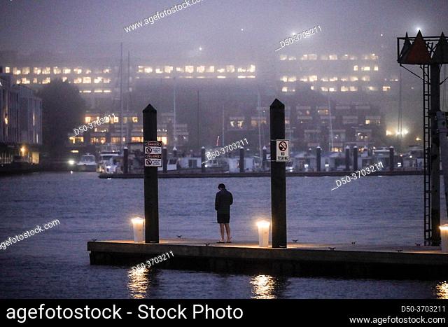 Boston, Massachusetts, USA A man stands at a wharf at night at LoPresti Park