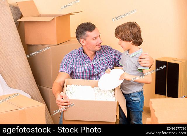 Father andhis little son unpacking boxes and moving into a new home. Little son taking different things from boxes