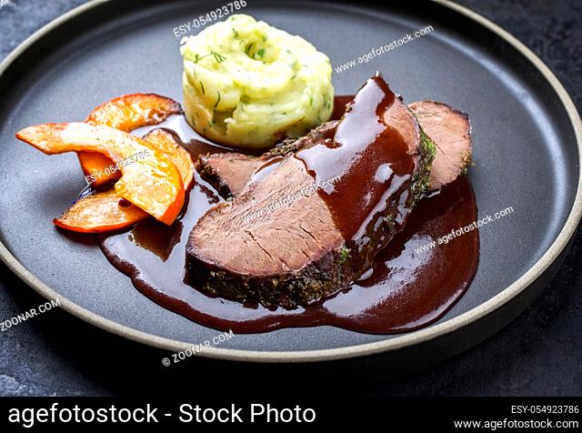 Traditional roasted beef heart with fried pumpkin slices and mashed potatoes in gravy red wine sauce as closeup on a modern design plate