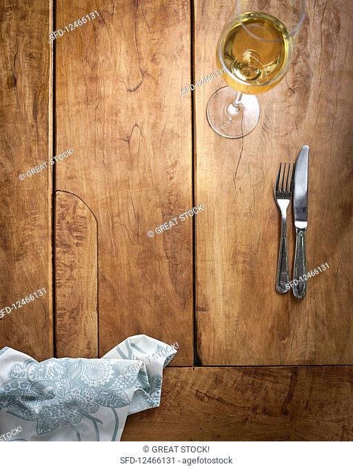 Cutlery and a glass of white wine on a wooden table