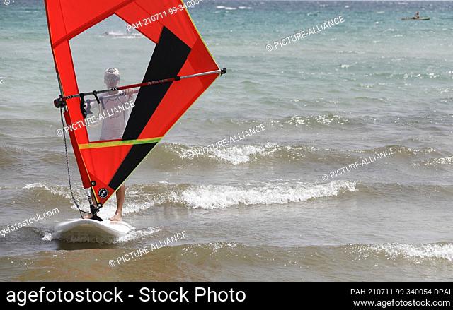 11 July 2021, Spain, -: Erik, an instructor at a water sports school, stands on a surfboard for a windsurfing lesson on the beach of Playa de Muro in the north...