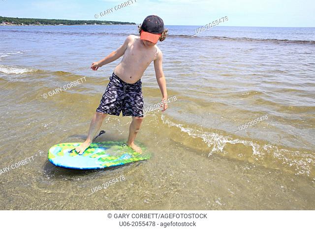 A 7 year old boy standing on a surf board in the waves at a beach at the sea