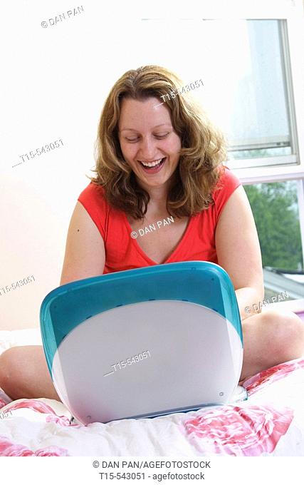 Caucasian woman in her 20's reading email laughing on bed in her bedroom