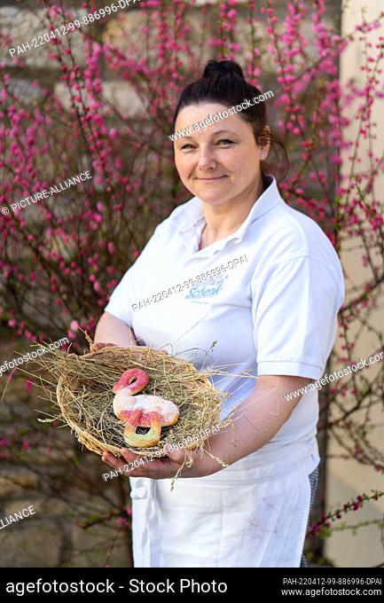PRODUCTION - 11 April 2022, Bavaria, Ostheim Vor Der Rhön: Master baker Juliane Witthauer holds an Easter nest with an ""Easter stork"" made from yeast dough...