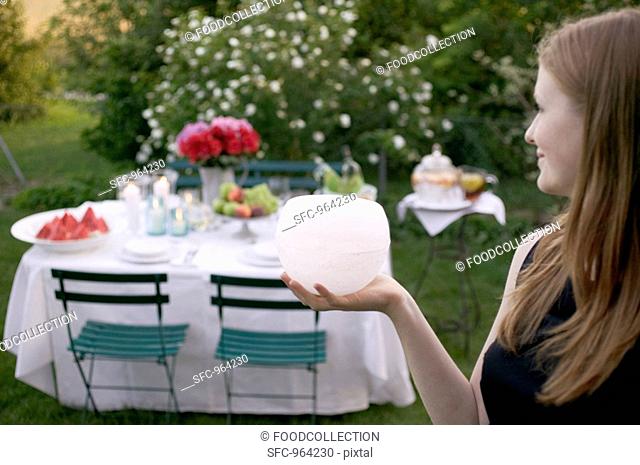 Woman holding windlight in front of table laid in garden