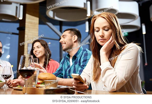 bored woman messaging on smartphone at restaurant