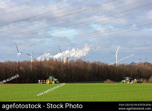 PRODUCTION - 29 December 2022, North Rhine-Westphalia, Bergheim: Tractors drive in a field while steam from the Neurath power plant rises behind trees