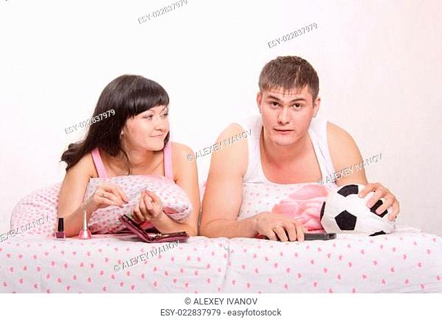 Husband watches football enthusiasm in bed, smiling wife