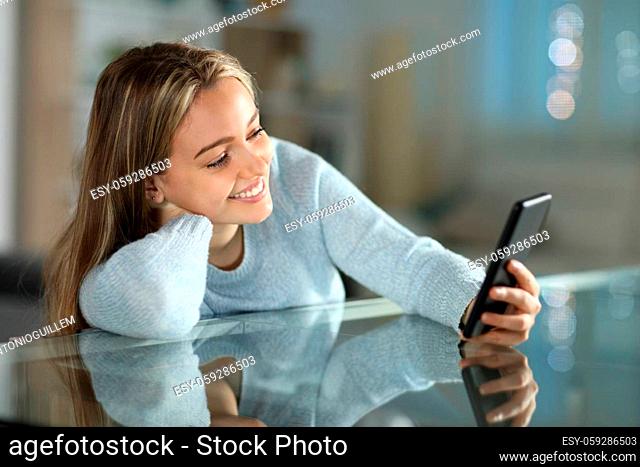 Happy teen using smart phone on a table in the living room at home in the night