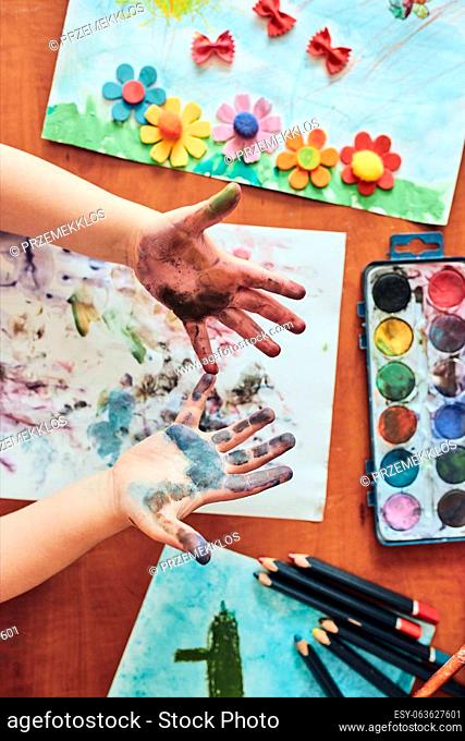 Little girl preschooler showing painted colourful hands. Child having fun making a stamps on sheet of paper with painted hands during an art class in the...
