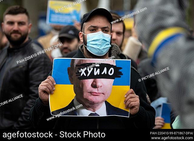 10 April 2022, Hessen, Frankfurt/Main: One word covers the eyes of Russian President Putin on his likeness in front of the Ukrainian flag on a poster with which...