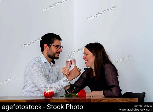 young couple toasting with pink champagne on valentine's day with candle and rose
