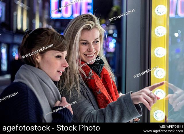 Smiling young women doing window shopping together at night