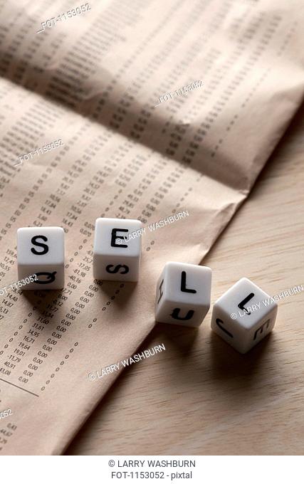 Lettered cubes spelling SELL lying on top of a financial page